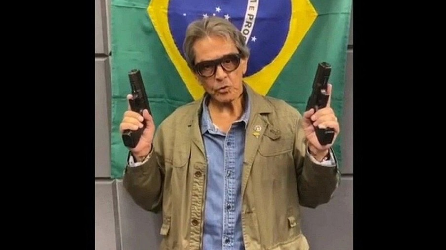Roberto Jefferson com armas e a bandeira do Brasil ao fundo | Divulgação