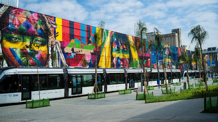 RIO DE JANEIRO, BRAZIL - 2016/07/29: Rio de Janeiro Light Rail ( Portuguese - VLT do Rio de Janeiro or VLT Carioca ), a light rail system opened in June 2016 ahead of the 2016 Olympic Games passes in front of Eduardo Kobra s Mural named Native people from the 5 continents ( Povos nativos dos 5 continentes ) at Boulevard do Porto in Rio de Janeiro port surrounding area, Brazil, part of the Porto Maravilha Project ( Marvelous Port Program ), a revitalization project of the city Port Zone. Kobra is a Brazilian street artist notable for painting large murals, usually depicting portraits with a technique of repeating squares and triangles, utilizing bright colors and bold lines while staying true to a kaleidoscope theme. (Photo by Ricardo Funari/Brazil Photos/LightRocket via Getty Images)